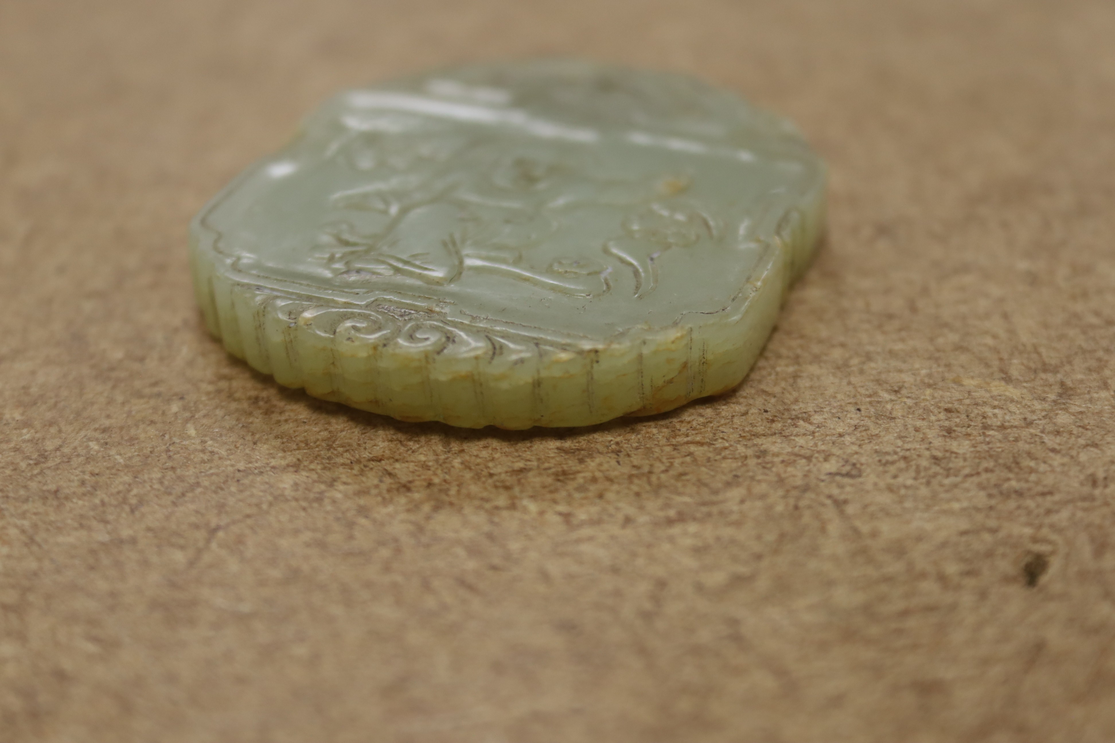 A Chinese pale celadon jade plaque, boy and bats, 5cm wide